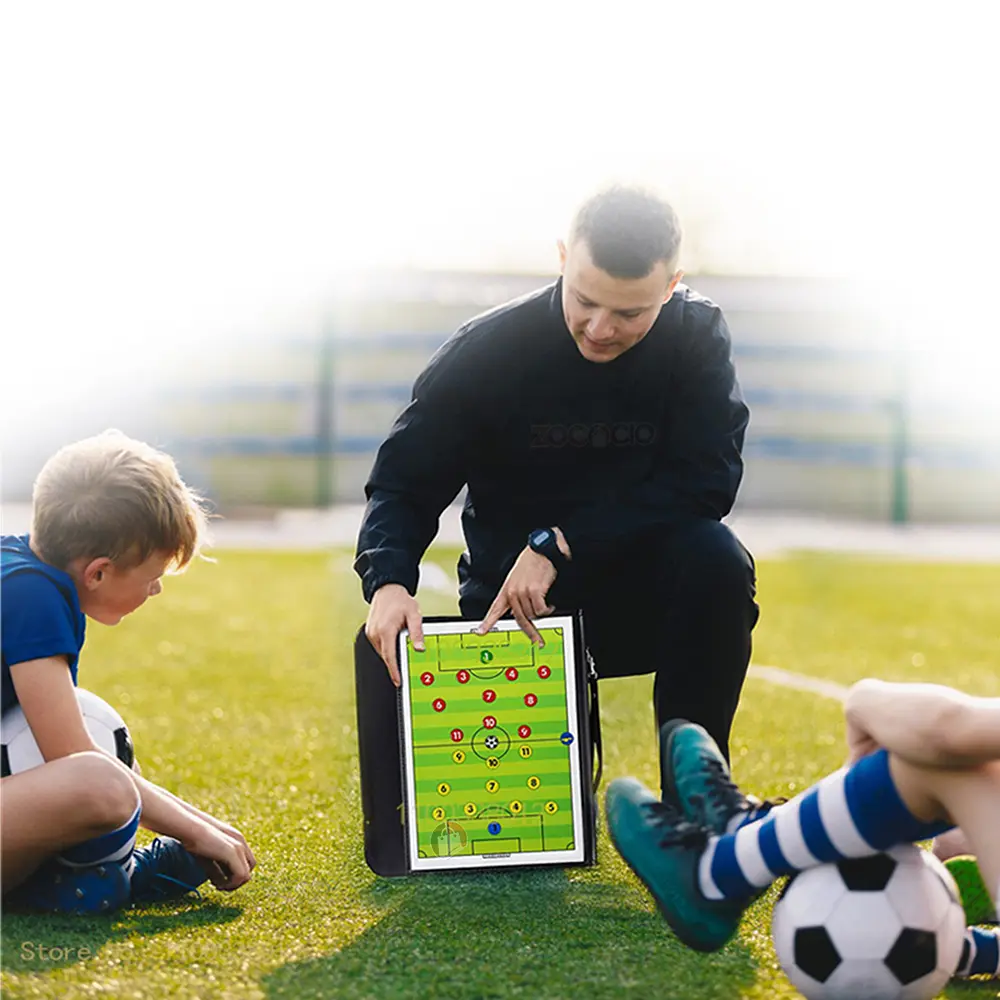 Tablero táctico de fútbol en carpeta, un entrenador explica la jugada a un niño en un campo de entrenamiento.