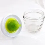 Brocha de silicona verde para cocina sobre mesa blanca junto a pequeño frasco de vidrio.