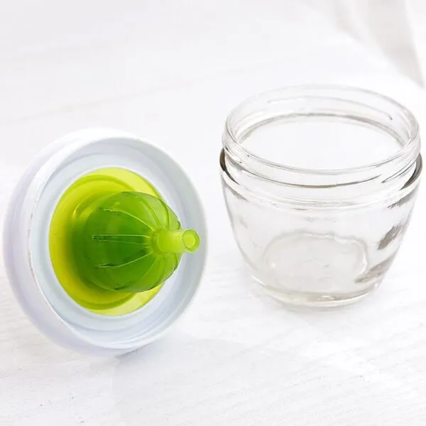 Brocha de silicona verde para cocina sobre mesa blanca junto a pequeño frasco de vidrio.