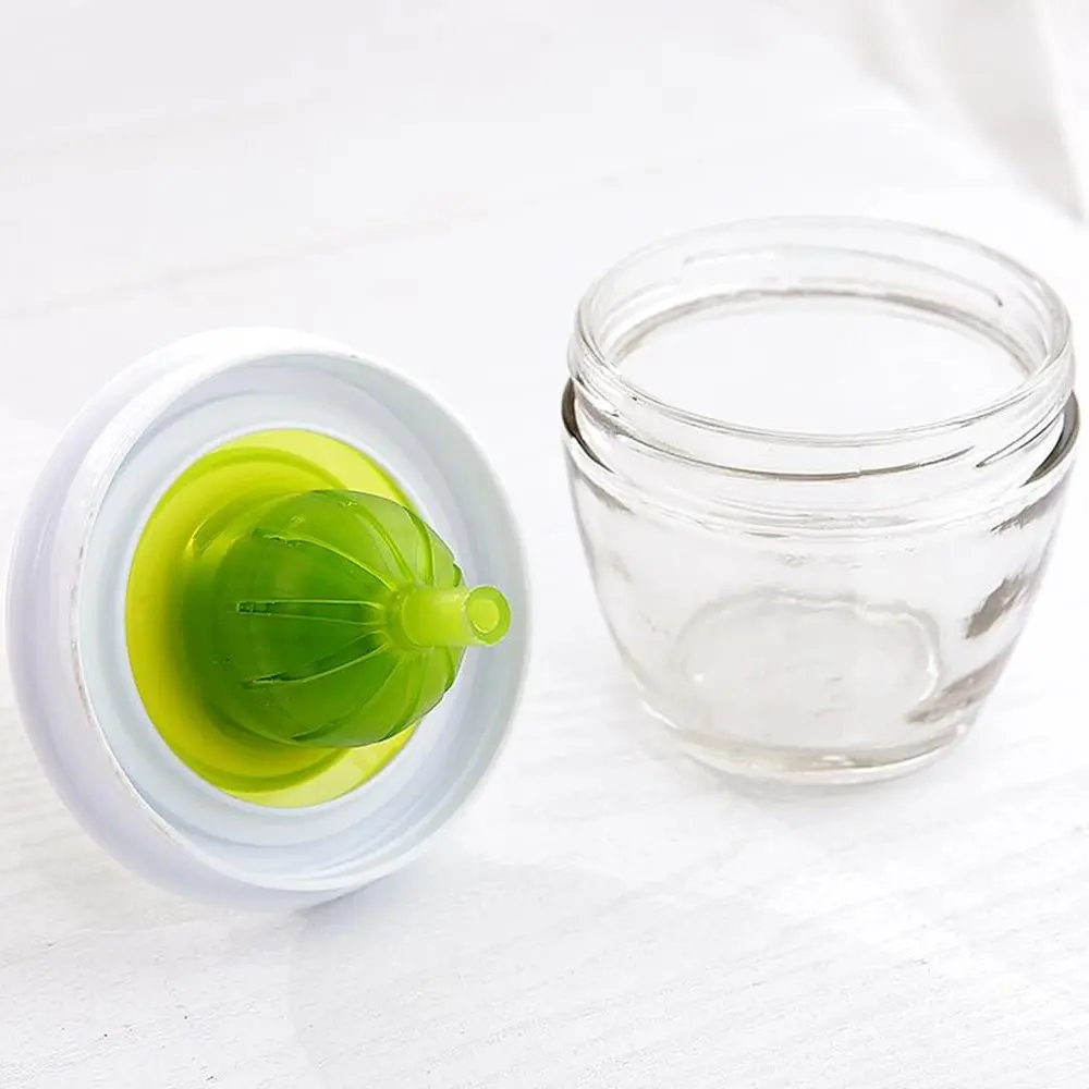 Brocha de silicona verde para cocina sobre mesa blanca junto a pequeño frasco de vidrio.