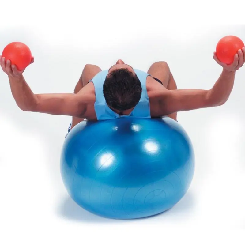 Hombre con balón de yoga azul, sosteniendo pelotas rojas, entrenando en gymball.
