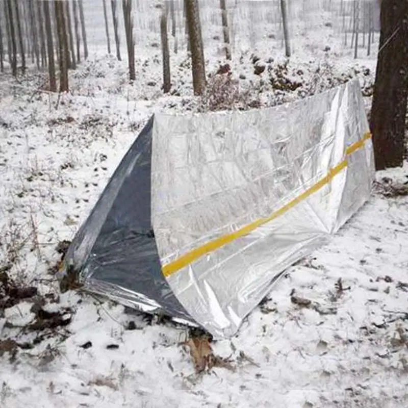 Carpa térmica plateada para camping y emergencias, ideal para temperaturas extremas en bosques nevados.