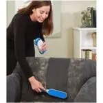 Cepillo removedor de pelos y motas limpiando un sofá oscuro con pelos de mascota.