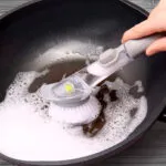 Cepillo con dispensador de jabón lavando un wok con abundante espuma.