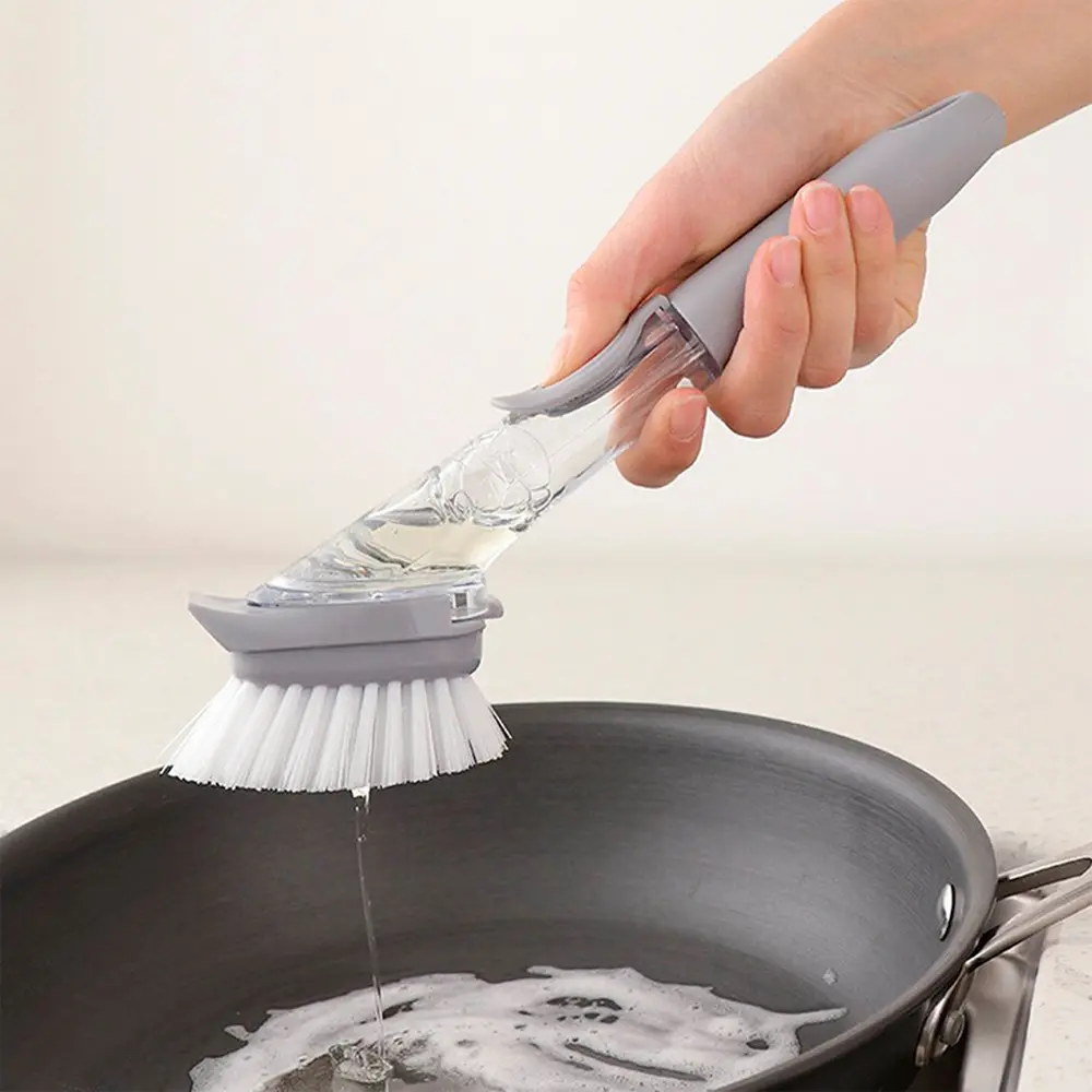 Cepillo con dispensador de jabón lavando sartén con espuma, para limpieza de cocina.