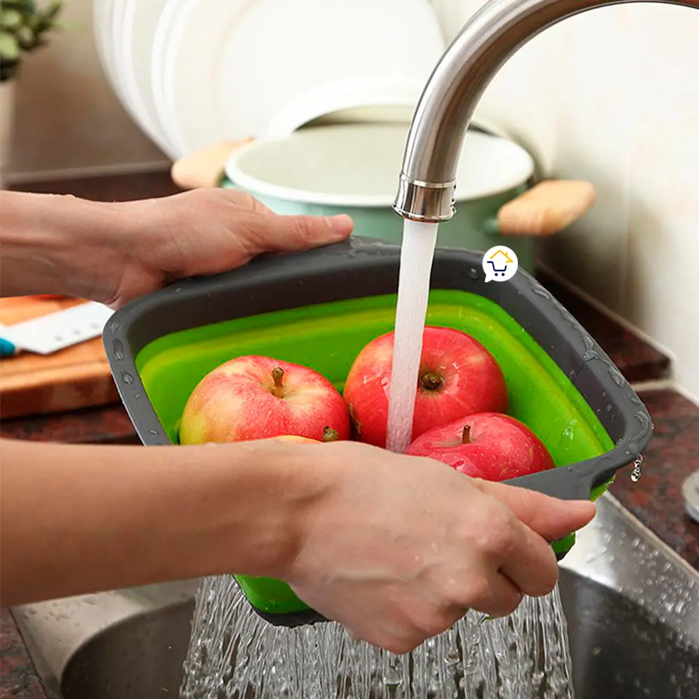 Colador plegable de silicona con manzanas bajo el chorro del grifo en la cocina.