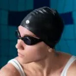 Nadadora con gorro de silicona, gafas y tapones en piscina, lista para competir.