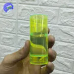 Set x12 copas tequileras neón reutilizables sostenidas en mano, con líquido amarillo brillante.