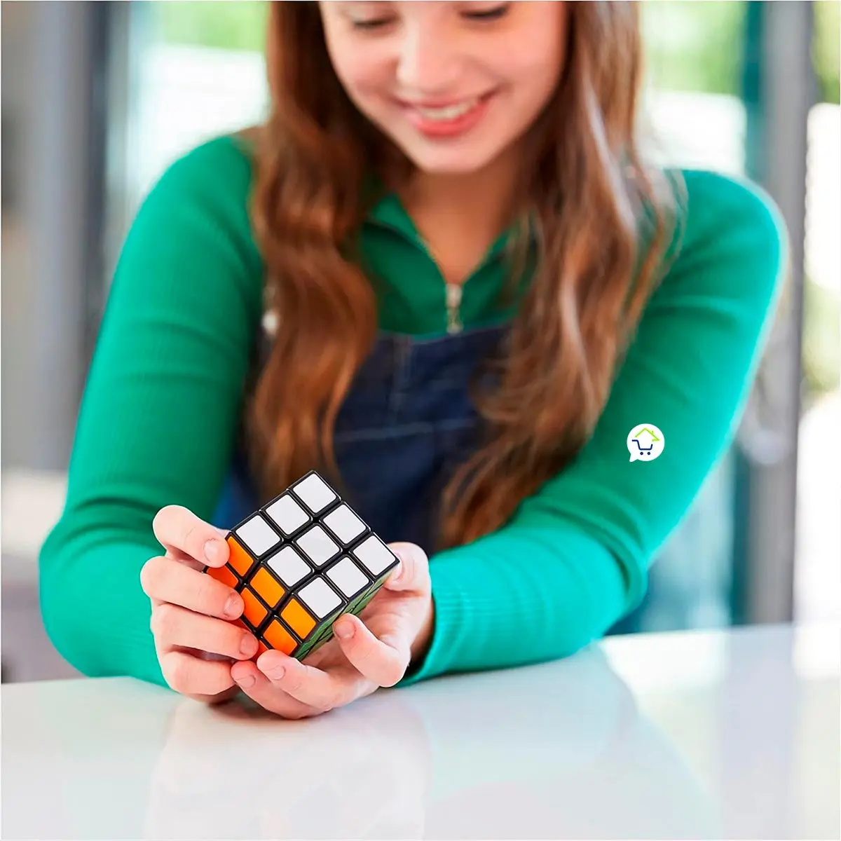 Niña sonriente jugando con cubo Rubik 3x3 en mesa blanca, con detalle de carrito de compras.