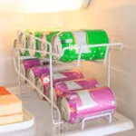 Dispensador de latas para nevera con bebidas verdes y rosadas en rack, ideal para refrigerador.