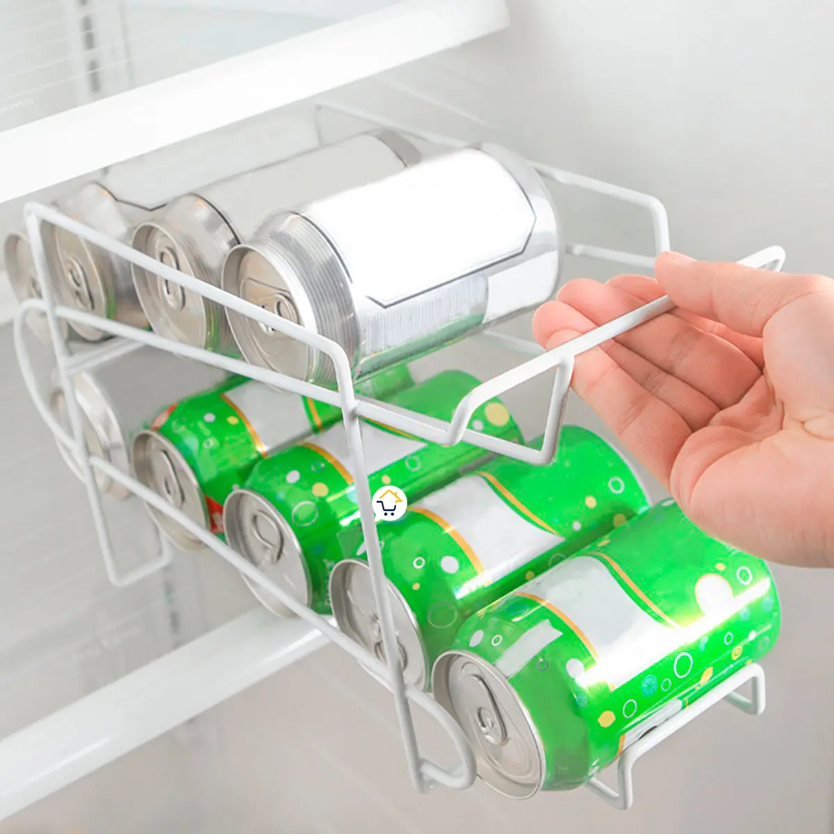 Dispensador de latas para nevera, con dos filas de bebidas plateadas y verdes, sostenido por mano.
