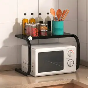 Estante organizador negro para microondas con frascos y utensilios de cocina sobre repisa.