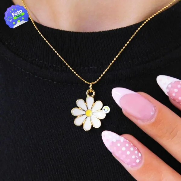 Collar de margarita dorada con esmalte blanco y amarillo, junto a uñas rosas con lunares blancos.