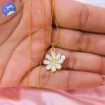Collar de flor de margarita con cadena dorada, presentado en una mano sobre fondo rosa.