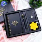 Kit de regalo para dama: cuaderno, collar con flor, vela amarilla y lapicero negro en caja.