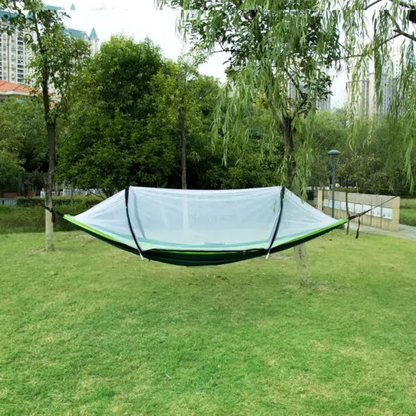 Hamaca de nailon con mosquitero, verde y blanca, suspendida entre árboles en un parque con césped.