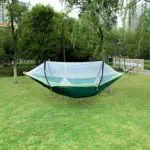 Hamaca de nailon verde con mosquitero, suspendidada entre árboles en un parque soleado.