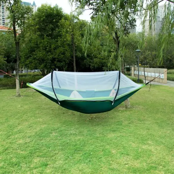 Hamaca de nailon verde con mosquitero, suspendidada entre árboles en un parque soleado.