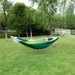 Hamaca de nailon verde y blanca con mosquitero, suspendida entre árboles en un parque.
