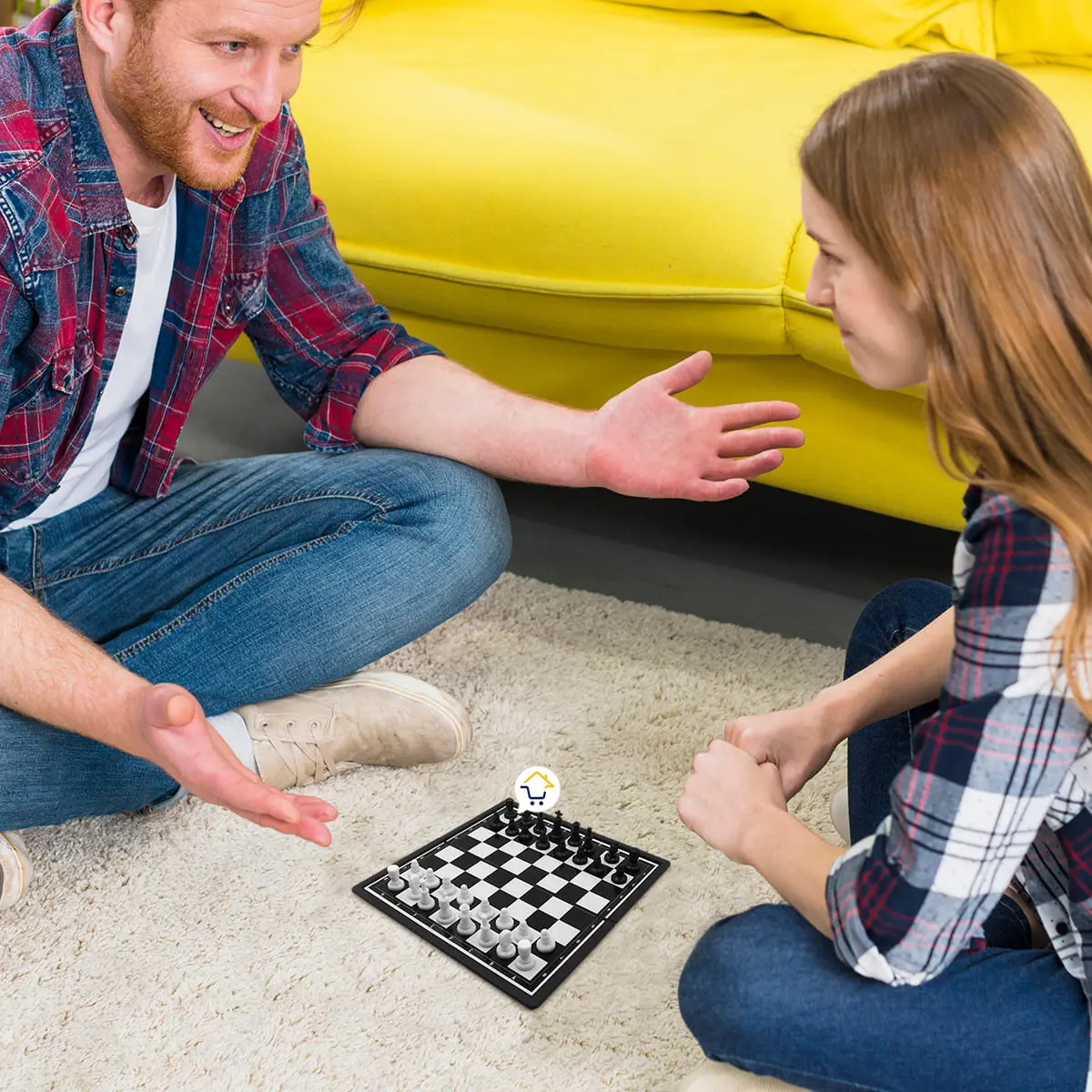 Hombre y mujer jugando mini ajedrez magnético portátil en el suelo junto a un sofá amarillo.