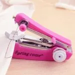 Mini máquina de coser de mano portátil rosa cosiendo tela blanca con hilo rojo.