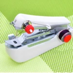 Mini máquina de coser de mano portátil blanca con hilo y carrete morado sobre fondo verde tejido.