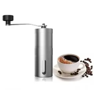 Molino manual de café en acero, molinillo portátil con manivela y taza de café al lado.