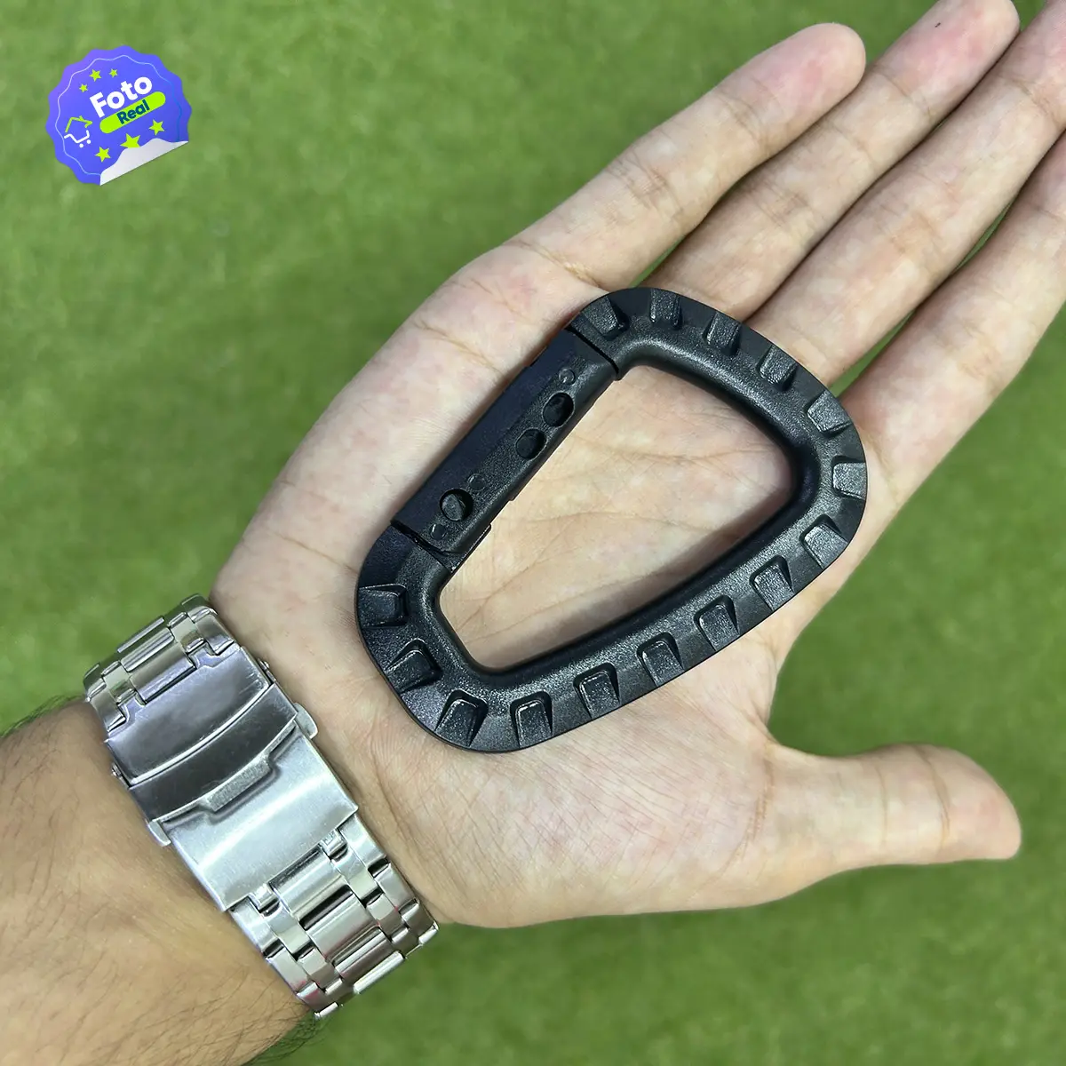 Mosquetón táctico negro en forma de D, sujeto en una mano con un reloj de plata.