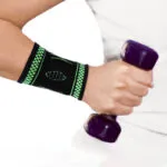 Muñequera elástica deportiva negra y verde para protección en gimnasio y ejercicio, sujetando pesa.