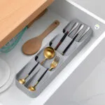Organizador de cubiertos dorado y plateado en cajón de cocina con utensilios de madera y batidor.