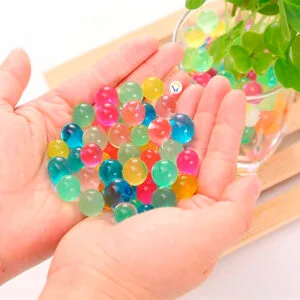 Manos sostienen perlas hidrogel decorativas de colores, brillantes y translúcidas.