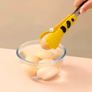 Pinza de cocina con diseño de patita de gatito amarilla sosteniendo un huevo sobre un bowl con huevos.