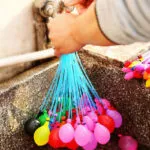 Set Magic Balloons recargando globos de agua de colores bajo un grifo.
