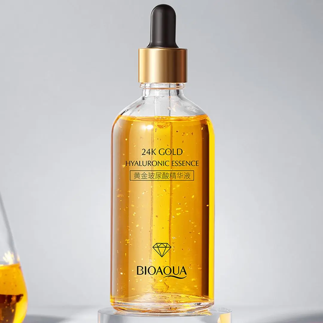 Serum Bioaqua 24K Gold Hyaluronic Essence con gotas doradas en frasco de vidrio transparente.