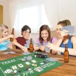 Set de póker Texas con tapete y barajas de cartas, gente jugando y sonriendo.