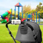 Soporte universal 360 para celular en manubrio de coche de bebé en parque infantil.