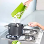 Tabla plegable verde verter champiñones picados en olla sobre estufa.