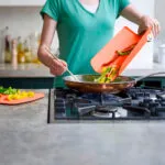 Tabla de cortar plegable volcando pimientos en sartén sobre estufa, cocina casera.