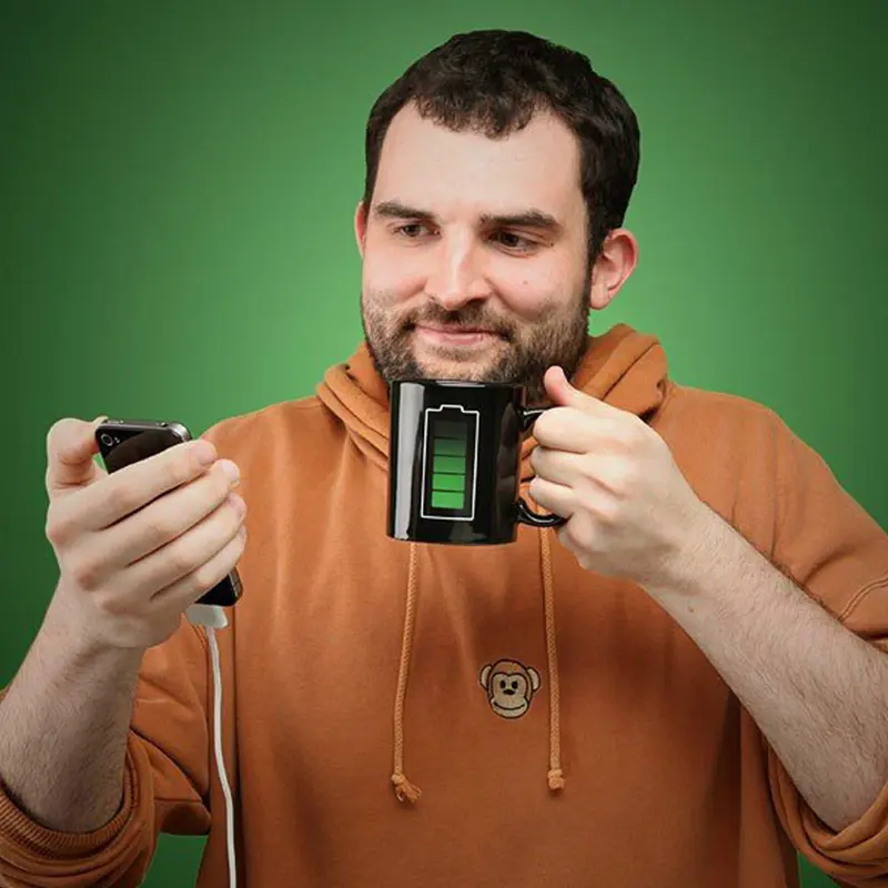 Hombre sostiene celular y taza mágica que cambia con el calor, con diseño de batería.
