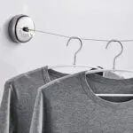 Tendedero retráctil de pared ajustable con dos camisetas grises colgadas.