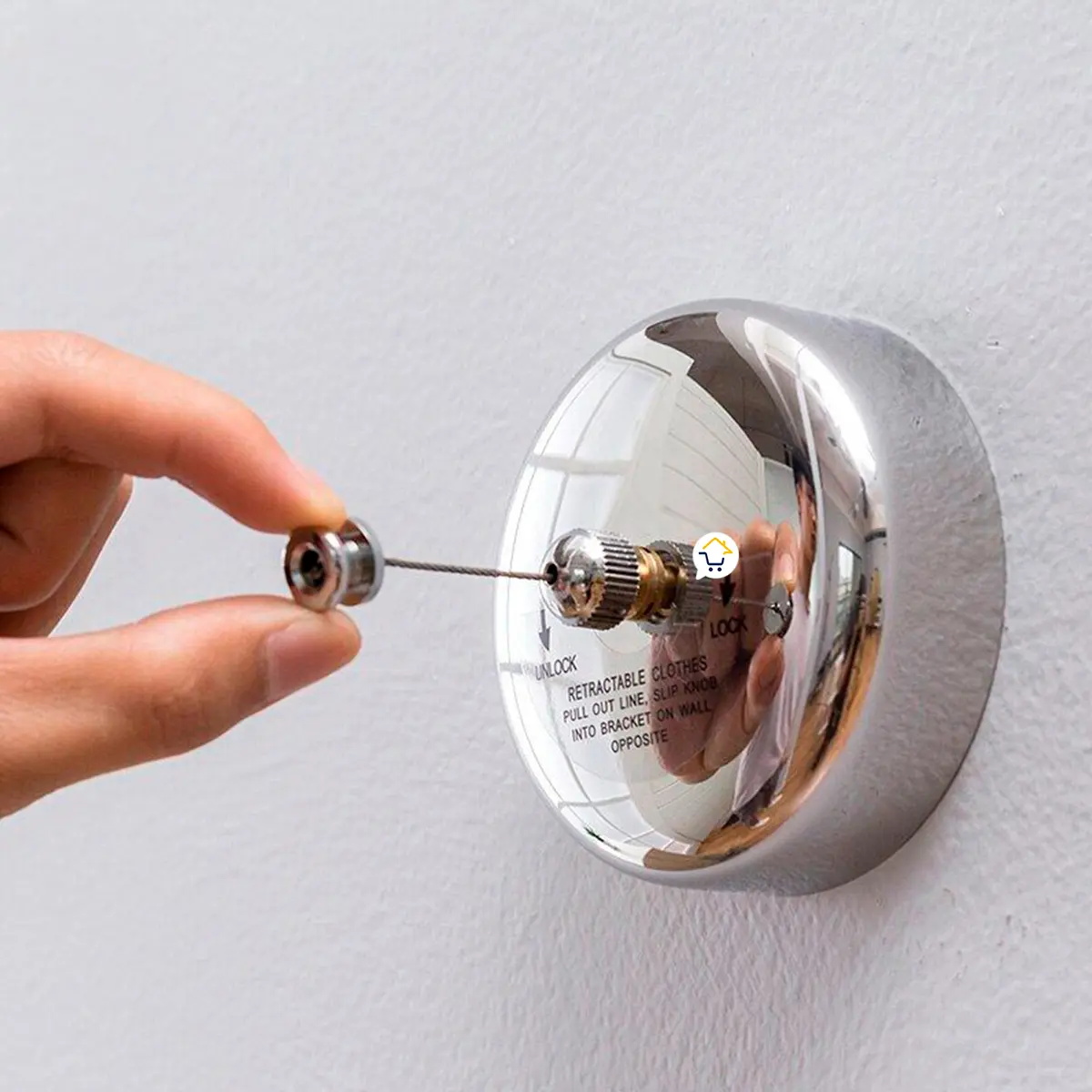 Tendedero retráctil de pared con hilo ajustable que una mano sujeta para colgar ropa.