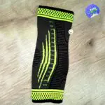 Tobillera de compresión deportiva ortopédica con diseño de rayas verdes sobre fondo gris.