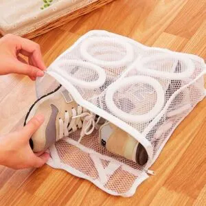 Bolsa de malla blanca para lavar zapatillas, con compartimentos para zapatos, en piso de madera.