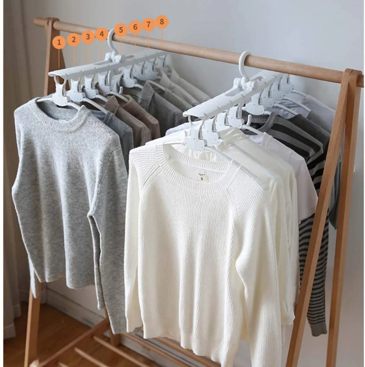 Perchero colgante ahorrador con 8 prendas de ropa, suéteres grises y blancos.