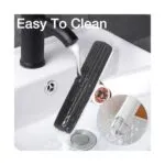 Mini trapeador de escritorio negro pasando bajo agua de grifo en lavabo blanco, fácil limpieza.