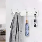 Perchero flotante blanco con 4 ganchos dobles, colgado con abrigo, paraguas azul y osito negro.