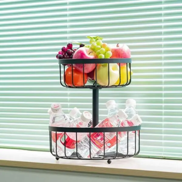 Estante organizador de 2 niveles con frutas y botellas de agua frente a persianas verdes.