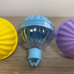 Set x4 moldes esféricos para hielo en silicona, uno amarillo, uno azul y uno morado, en mesa de madera.
