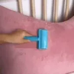 Rodillo quitapelusas azul sobre almohada rosa, ideal para hogar y mascotas.