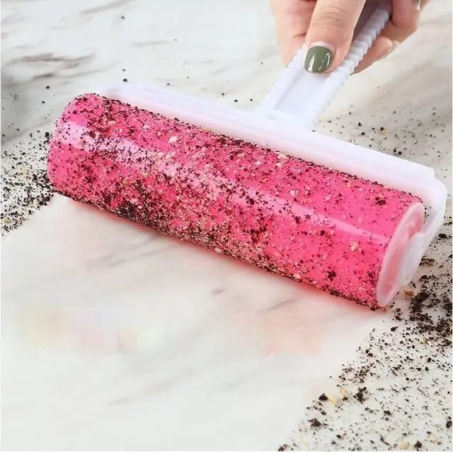 Rodillo de pelusa reutilizable y lavable rosado recogiendo suciedad y migas de una superficie clara.
